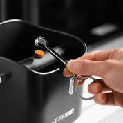 Kaffee-Schlüsselanhänger in Form eines Siebträgers an einem Abklopfbehälter