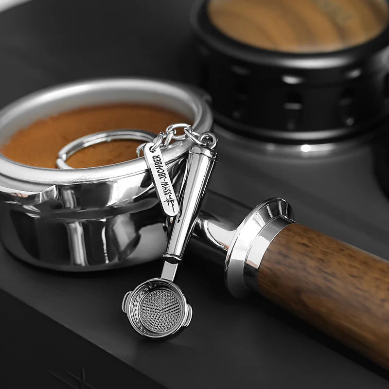Kaffee-Schlüsselanhänger in Form eines Siebträgers neben Espressomaschine und Tamper