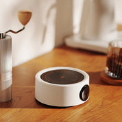 Elektrischer Kaffeewärmer in Weiß auf einem Holztisch neben Kaffeezubehör