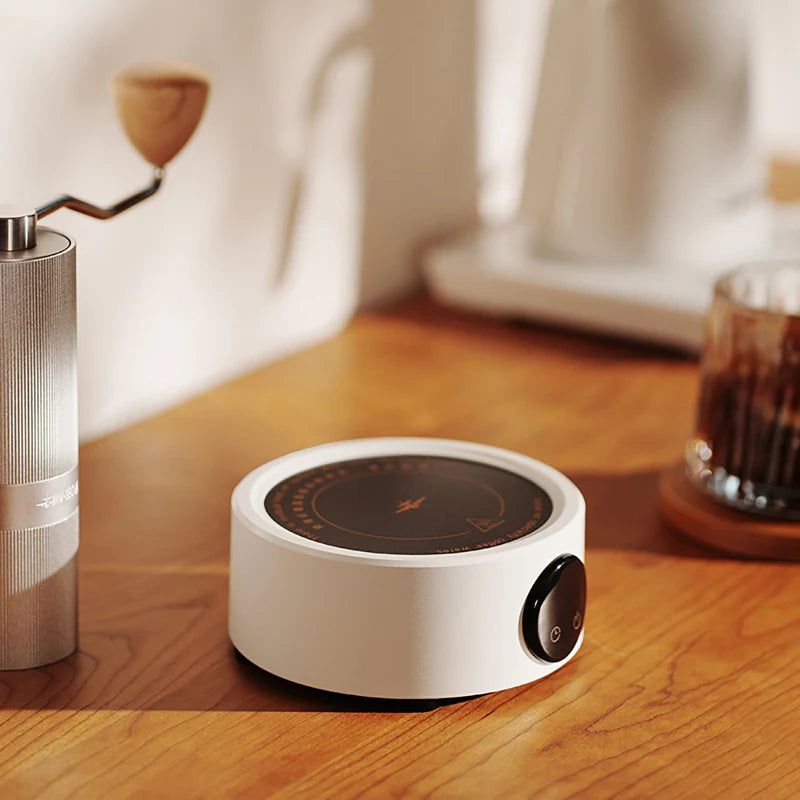 Elektrischer Kaffeewärmer in Weiß auf einem Holztisch neben Kaffeezubehör